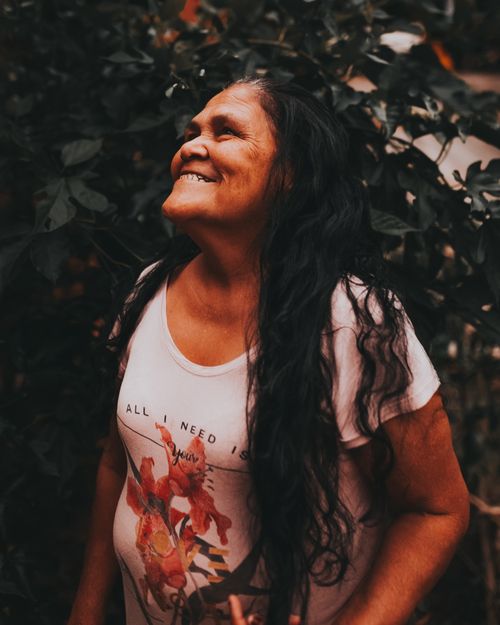 Free Portrait of a joyful elderly woman with long dark hair smiling outdoors amidst lush greenery. Stock Photo