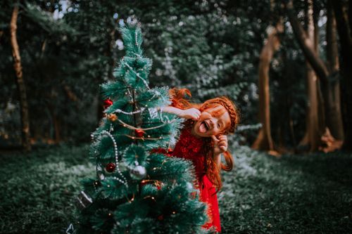 Free Red-haired girl playfully posing with a decorated Christmas tree in the forest. Stock Photo