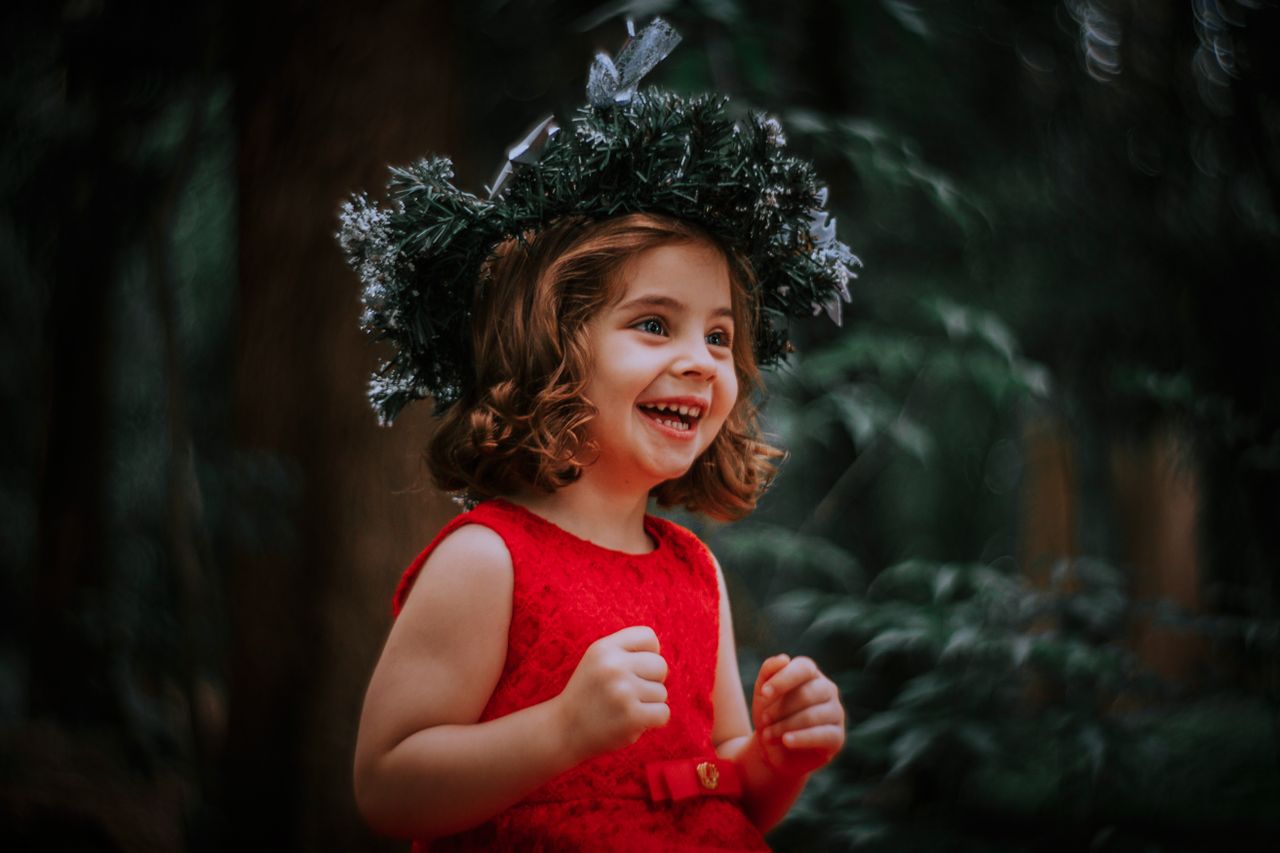 smiling child in a red dress adorned with a festive wreath capturing h