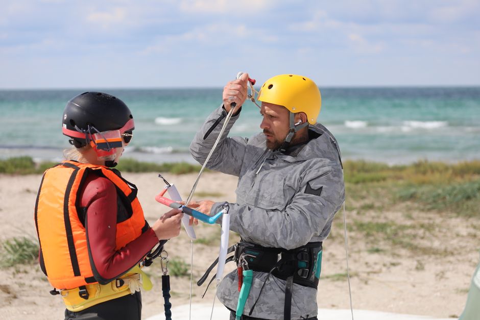 Two adults preparing for paragliding on a scenic seashore, emphasizing safety and teamwork.