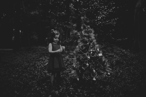 Black and White Photo of a Girl Standing Beside Christmas Tree