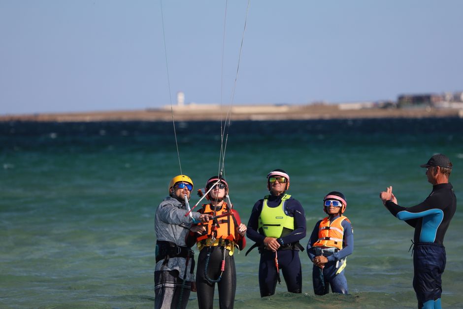 Group learning kitesurfing in shallow ocean waters under clear skies with instructor.