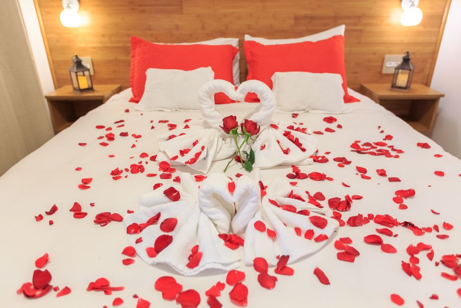 Quarto de hotel de luxo com pétalas de rosa e cisnes de toalha, ideal para casais em lua de mel.
