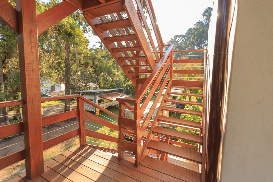 Wooden staircase basking in sunlight, surrounded by lush trees in an outdoor park setting.