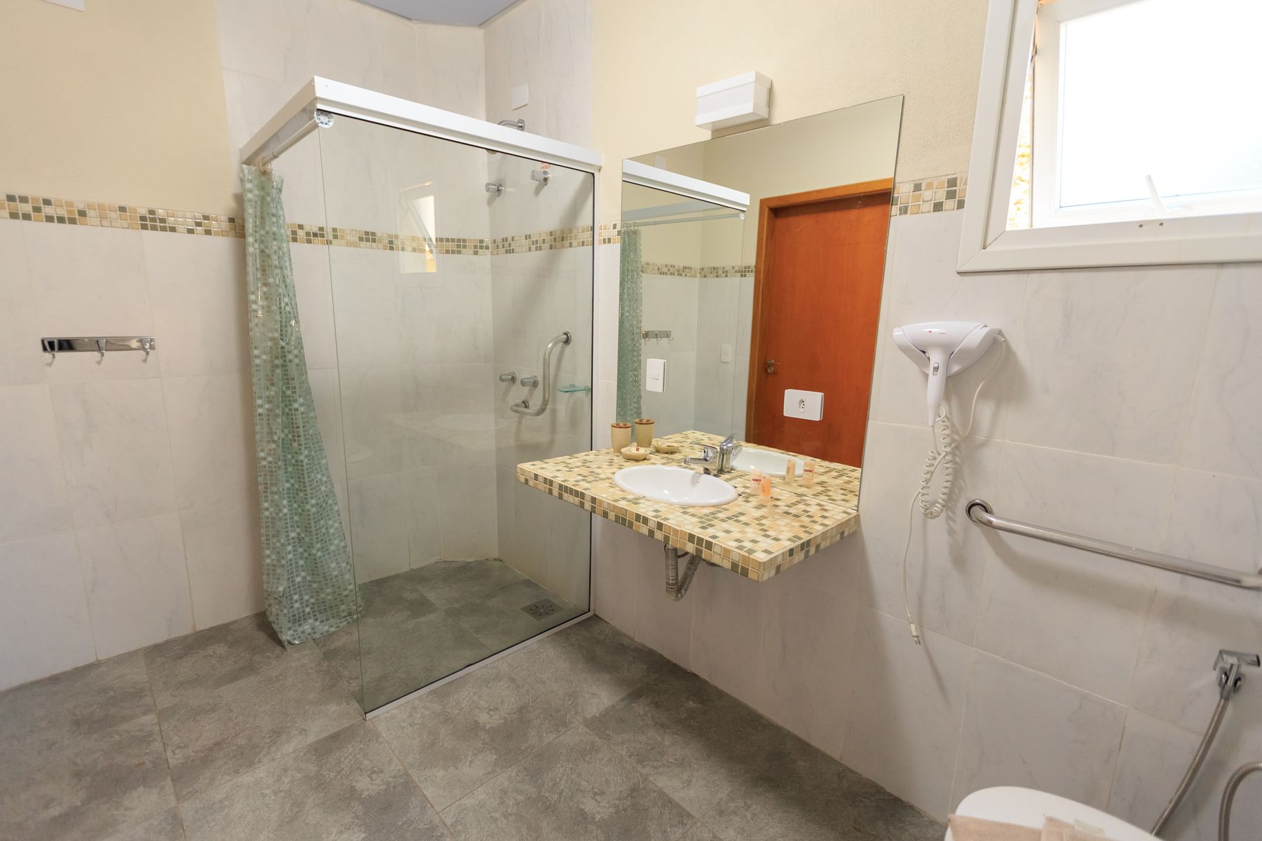 Accessible contemporary bathroom with an open shower, clear floor area, wall-mounted basin and visible grab rail