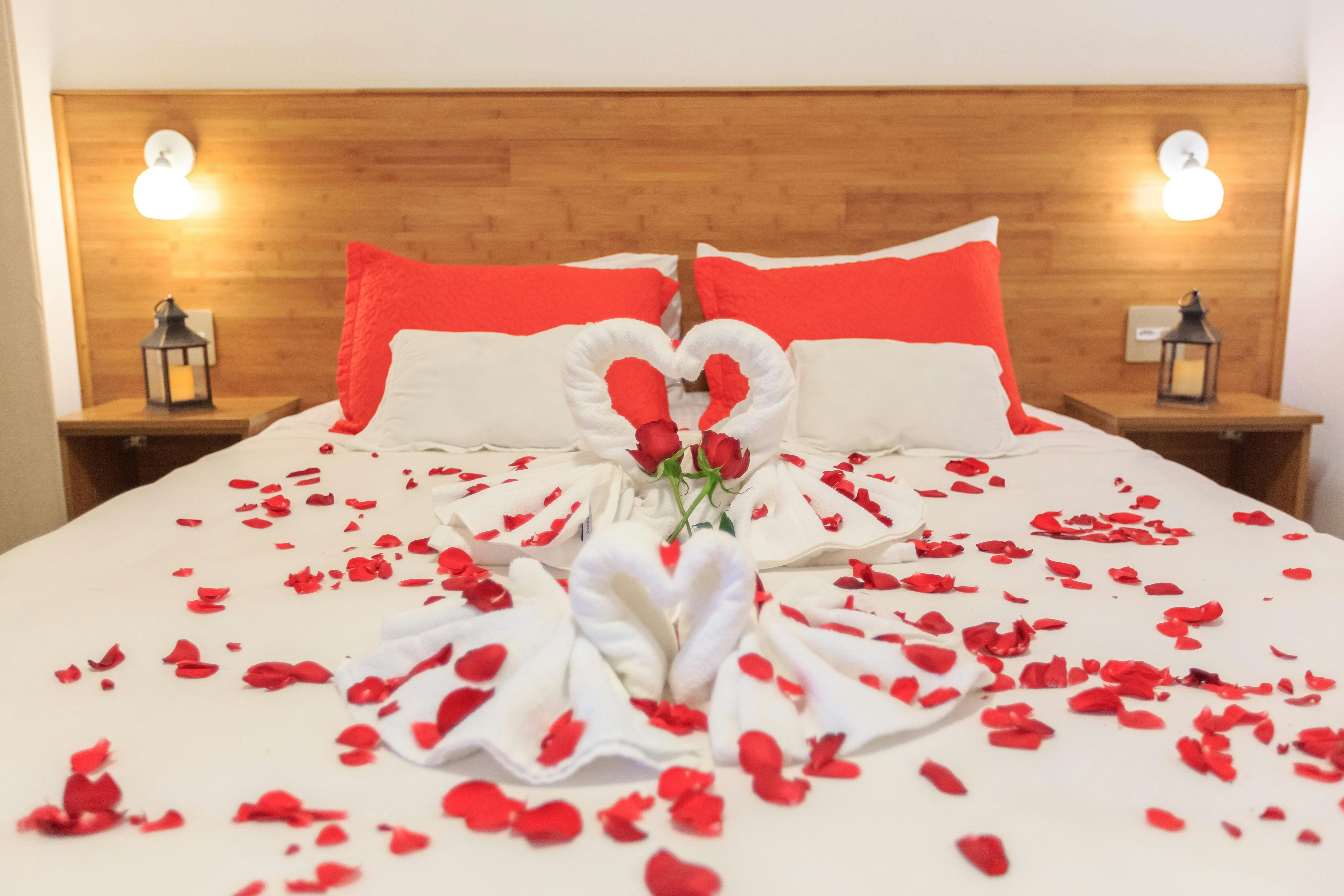Elegant hotel bedroom adorned with rose petals and towel swans, creating a romantic atmosphere.