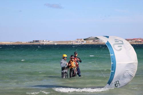 Free Two adults learn kitesurfing on a windy beach, guided by an instructor. Safety gear is visible. Stock Photo