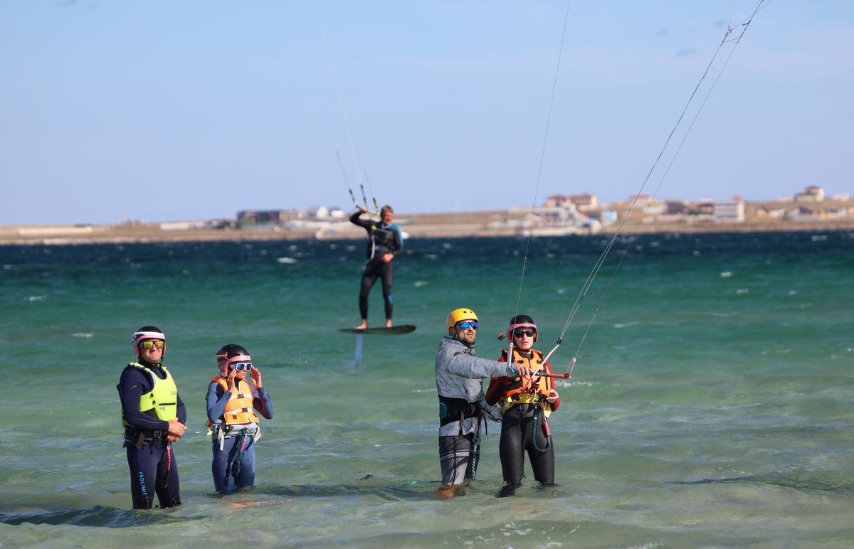Kitesurfing instructors teaching students in shallow sea water on a sunny day with safety equipment
