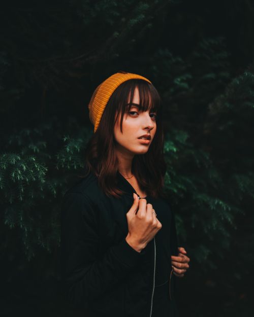 Free Portrait of a fashionable woman wearing a yellow beanie in a forest setting, exuding elegance and style. Stock Photo