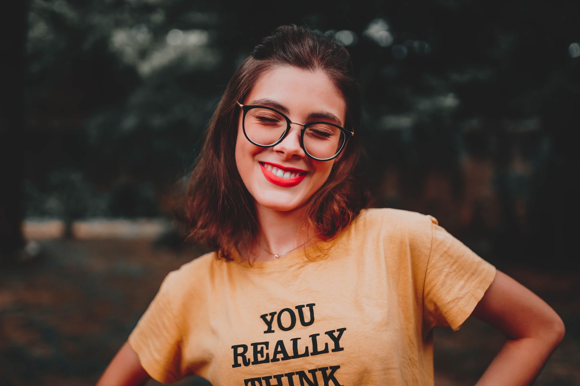 Happy woman with glasses and brown hair smiling while outdoors in a yellow shirt.