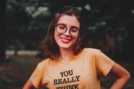 Happy woman with glasses and brown hair smiling while outdoors in a yellow shirt.