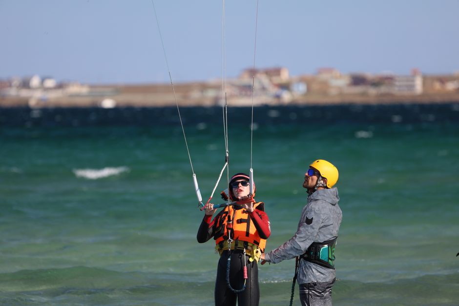 Instructor guiding kitesurfing lesson on a sunny day at the seaside. Safety gear emphasized.