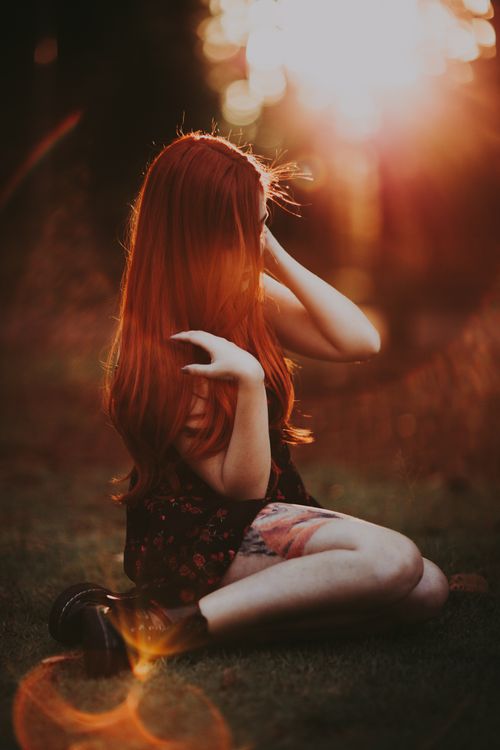 Free A woman with long red hair sits in a sunlit meadow, basking in the warm glow. Stock Photo
