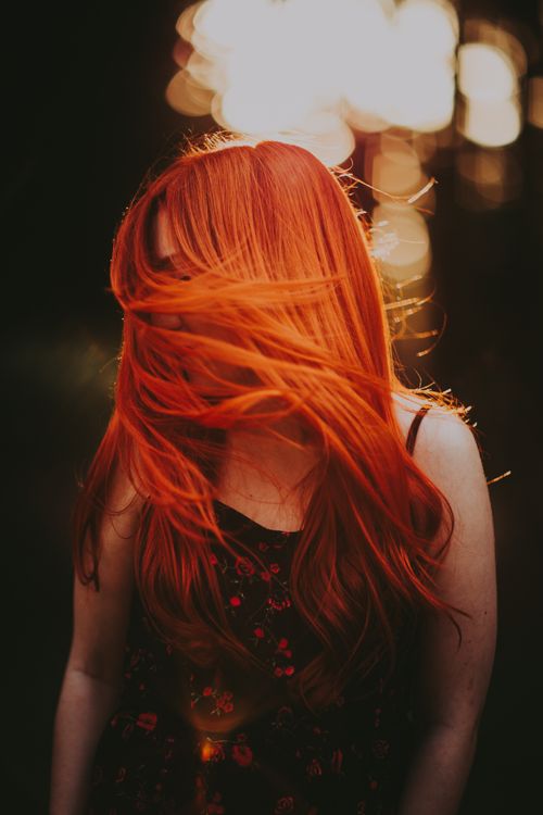 Free Candid photo of a woman with vibrant red hair captured in a whimsical outdoor setting. Stock Photo