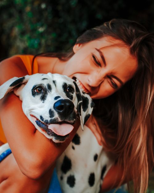Free A woman joyfully embraces her Dalmatian dog in a vibrant outdoor setting, capturing a moment of happiness. Stock Photo