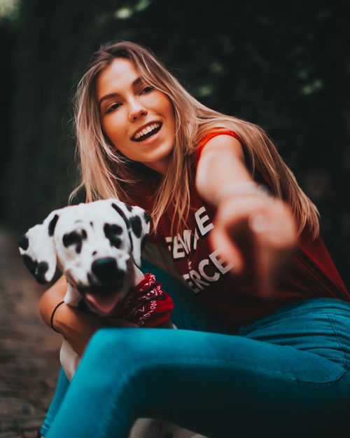 Free Happy woman with a Dalmatian dog pointing forward in a joyful outdoor scene. Stock Photo