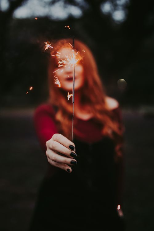 Free A woman holds a lit sparkler outdoors, creating a festive and warm atmosphere. Stock Photo