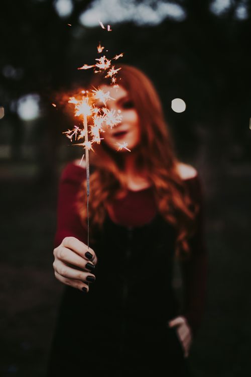 Free A redhead woman smiling while holding a lit sparkler during a nighttime celebration. Stock Photo