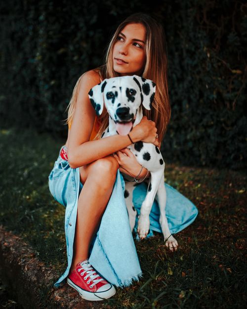 Free A young woman embraces her Dalmatian dog in a grassy outdoor setting, showcasing love and companionship. Stock Photo