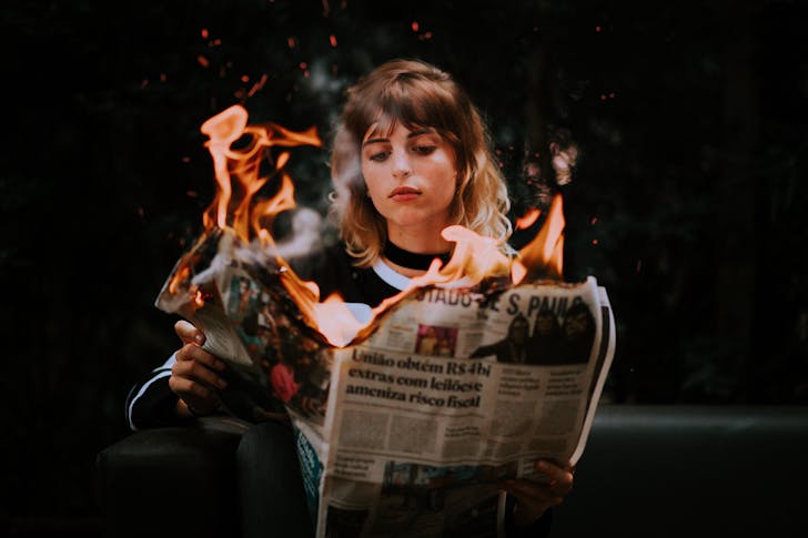 Woman Sitting and Reading Latest News in Burning Daily Paper