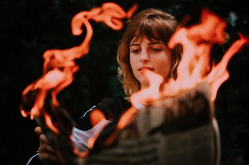 Free A woman intently watches flames consume a newspaper in an intriguing, dark atmosphere. Stock Photo