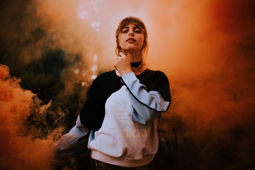 Portrait of a woman in sportswear surrounded by vibrant smoke, creating a dramatic and artistic look.