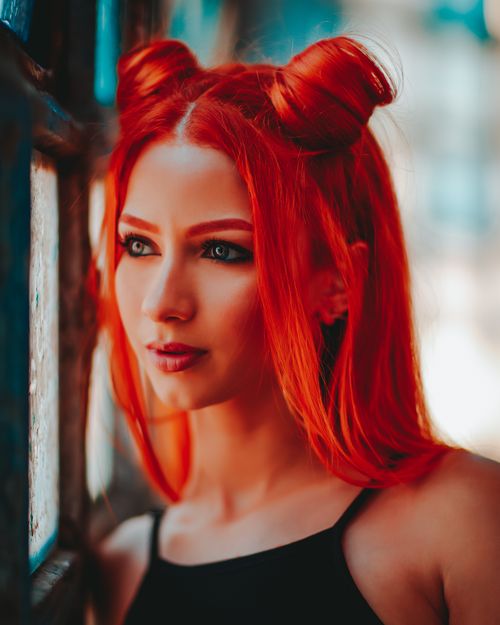 Free Portrait of a striking redhead woman with vibrant hair near a window. Stock Photo