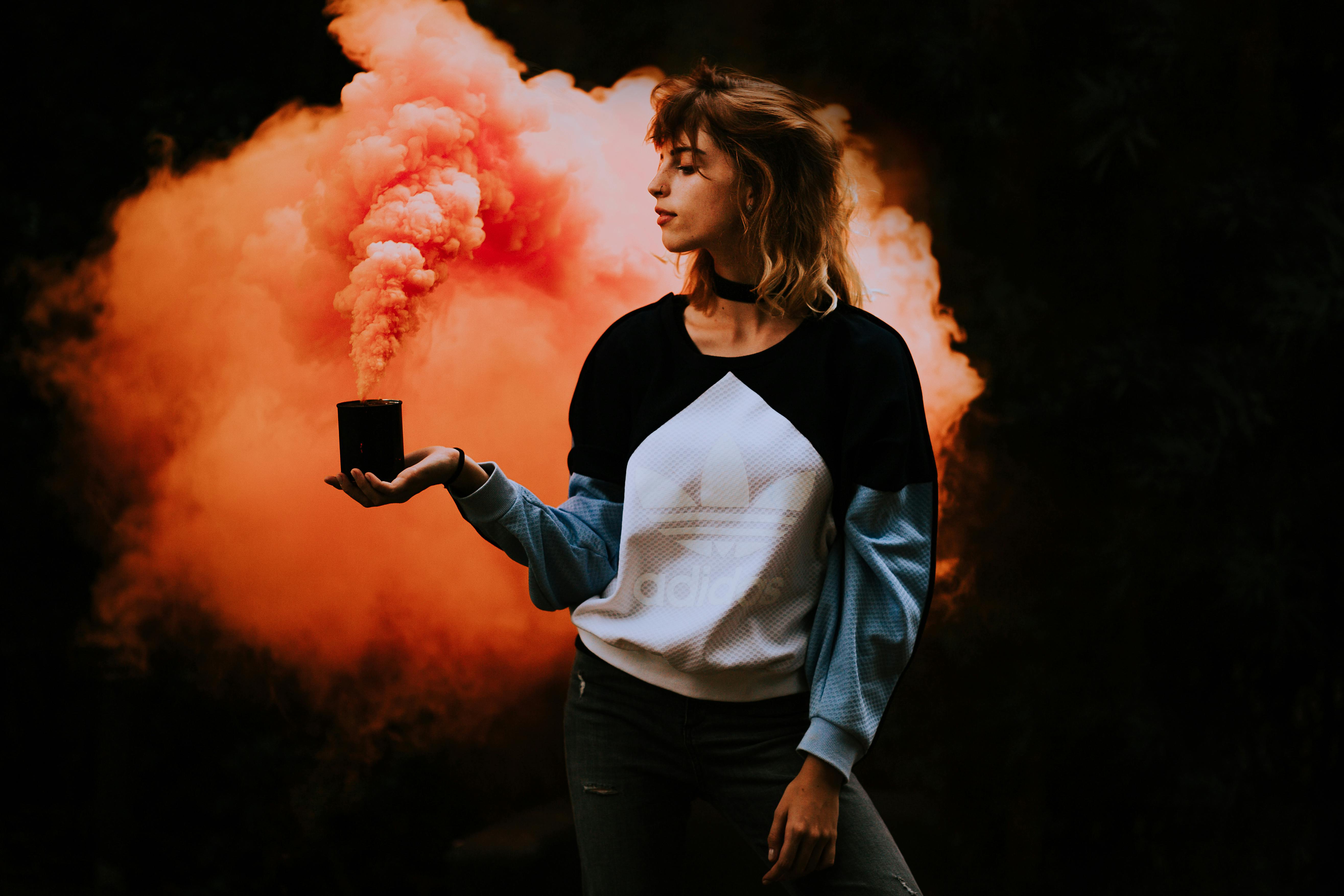 young woman in sweatshirt looking at lit smoke candle