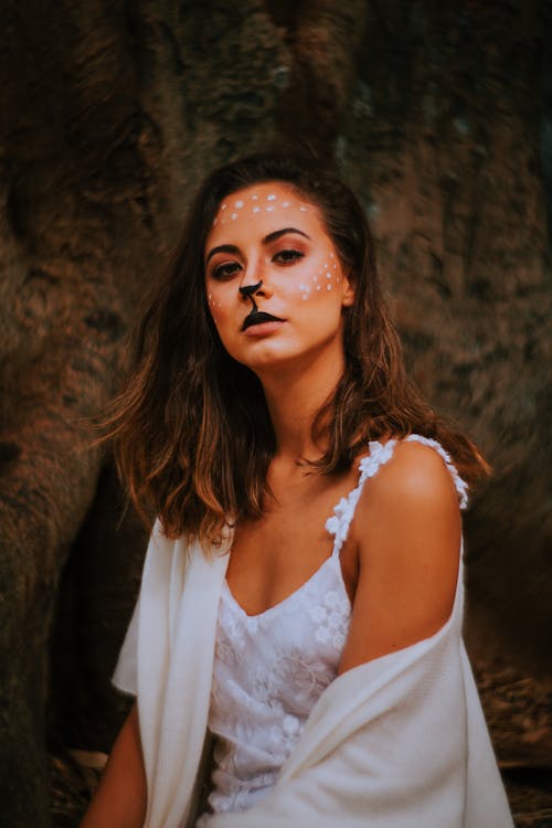 Woman With Her Face Painted Like a Deer Sitting in a White Dress 