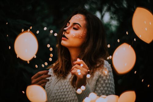 Free Young woman with fox-inspired face paint surrounded by warm lights. Stock Photo