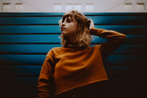 Free Artistic portrait of a woman in a rust-colored sweater against a blue backdrop, striking a thoughtful pose. Stock Photo