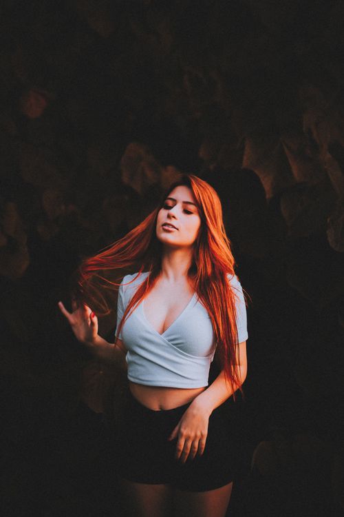Free A striking portrait of a red-haired woman in a crop top with her eyes closed against a dark background. Stock Photo
