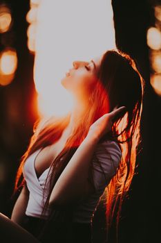 Redhead woman enjoys golden hour light, backlit by sunset in woodland setting.