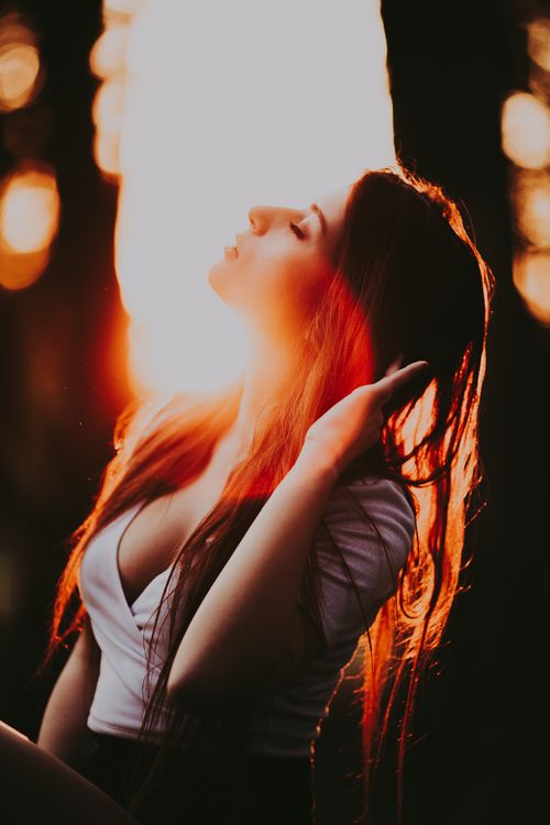 Free Redhead woman enjoys golden hour light, backlit by sunset in woodland setting. Stock Photo