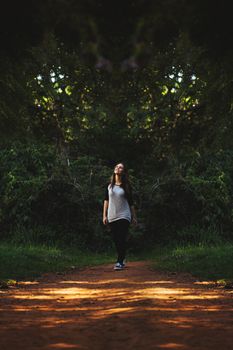 Young woman strolling on a serene forest path surrounded by lush greenery.