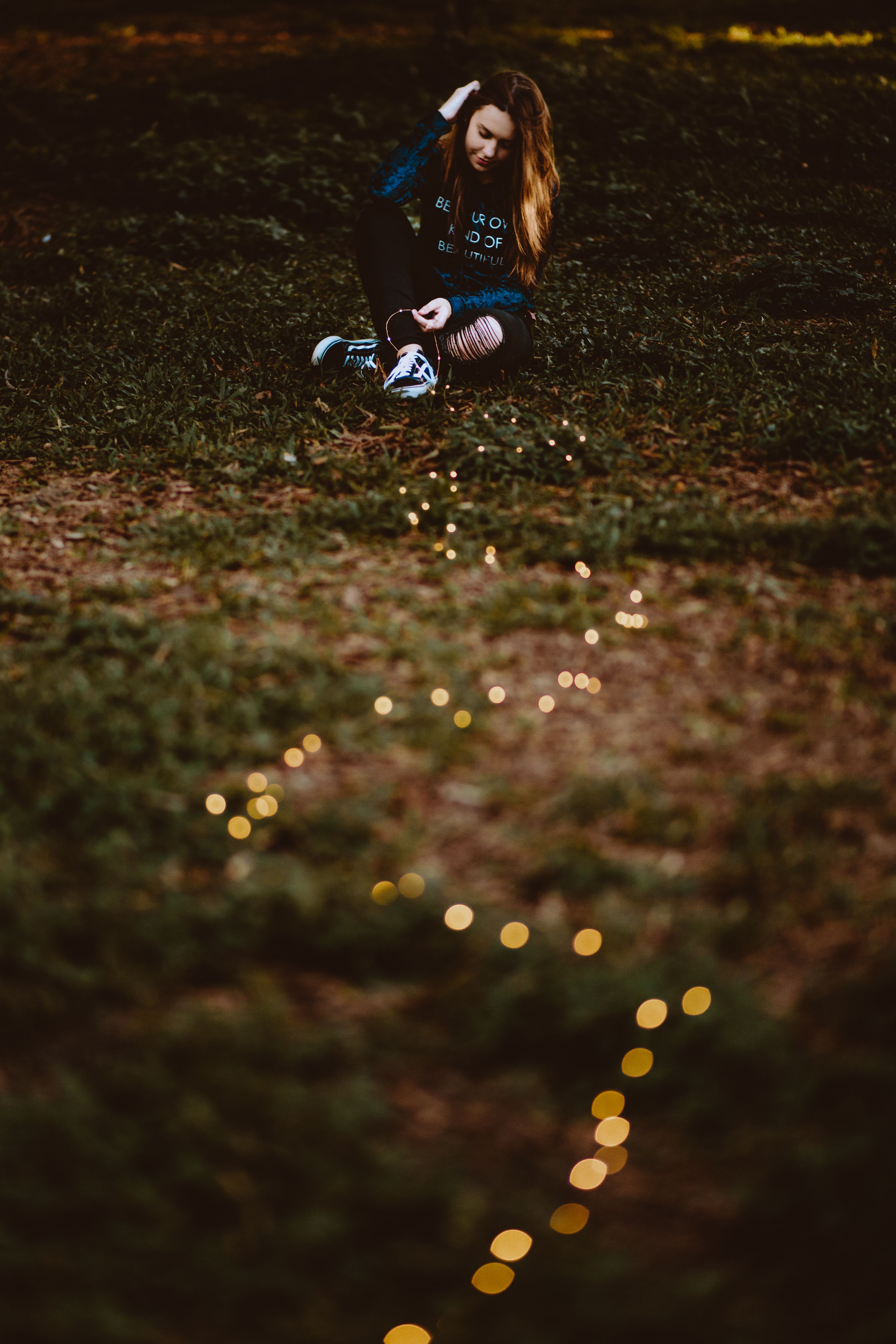 Young woman in a garden wearing a blue sweater with string lights on grass.