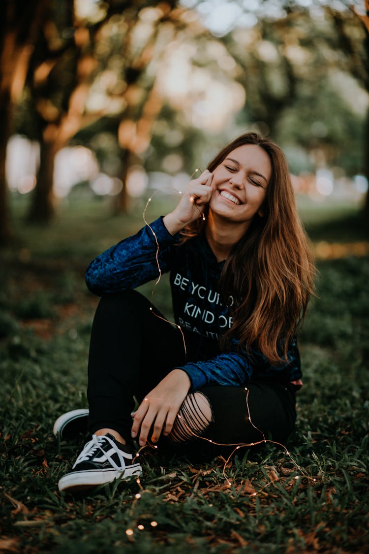 Young Woman Sitting On The Ground Smiling And Squinting 