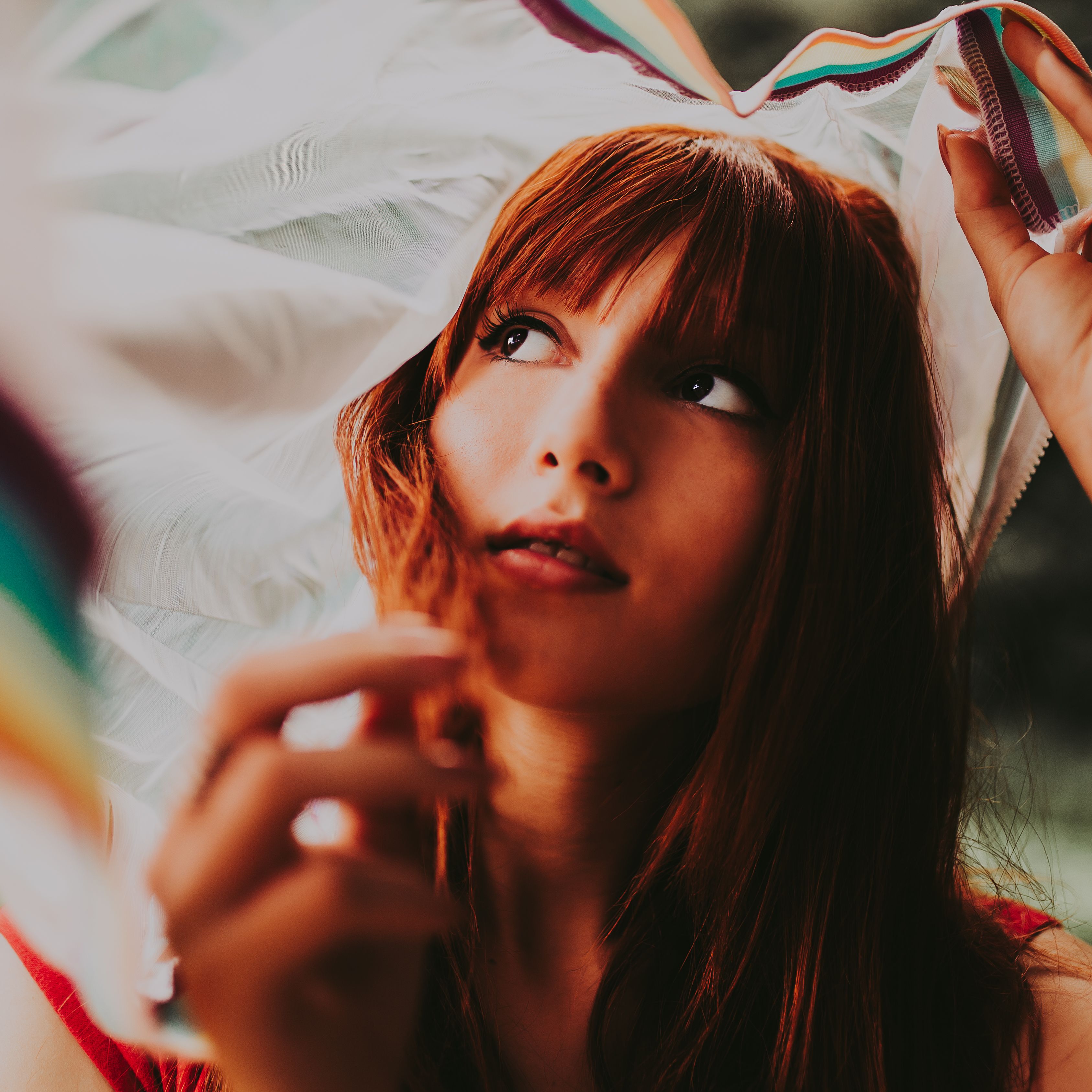 Beautiful portrait of a redheaded woman with a dreamy expression under a fabric outdoors.