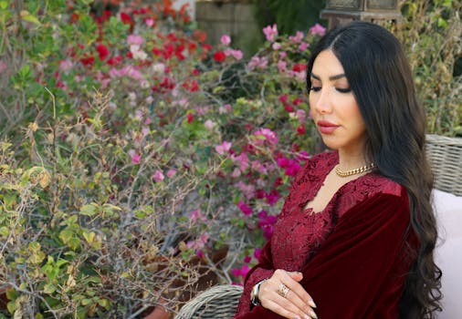 A woman in a burgundy dress sits gracefully in a lush garden in Dubai.