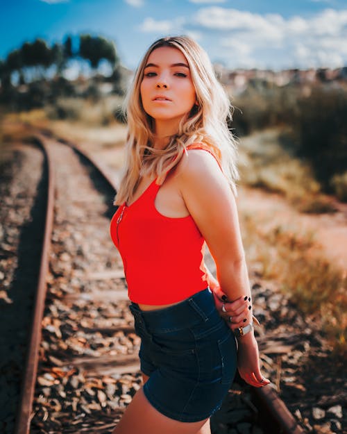 A Woman in Red Tank Top and Denim Shorts Standing at the Railway