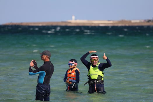 Three people enjoying kiteboarding in shallow sea water with helmets and life vests.