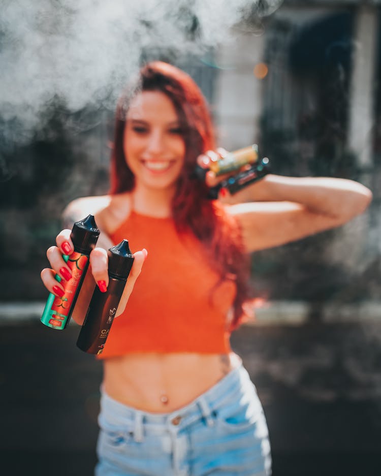 A Woman In Orange Tank Top Holding A Bottles Of Vape Juice