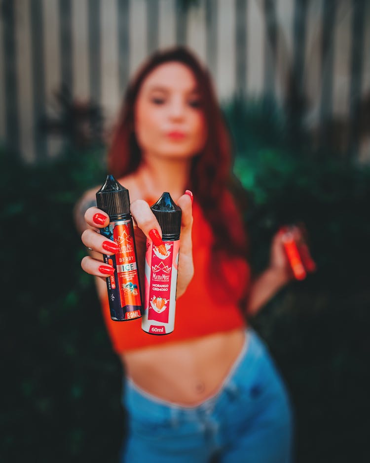 Woman Wearing Red Blouse And Red Manicure Presenting Plastic Bottles To The Camera