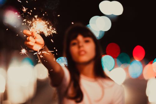 Free A young woman holding a sparkler with colorful bokeh lights in the background. Stock Photo