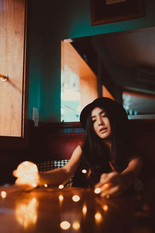 Free A woman sitting indoors with soft warm lights and a stylish hat in a cozy setting. Stock Photo