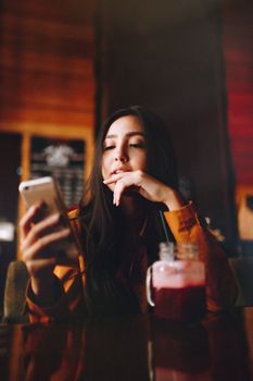 Young woman enjoying a drink while using her phone, sitting inside a cozy cafe.