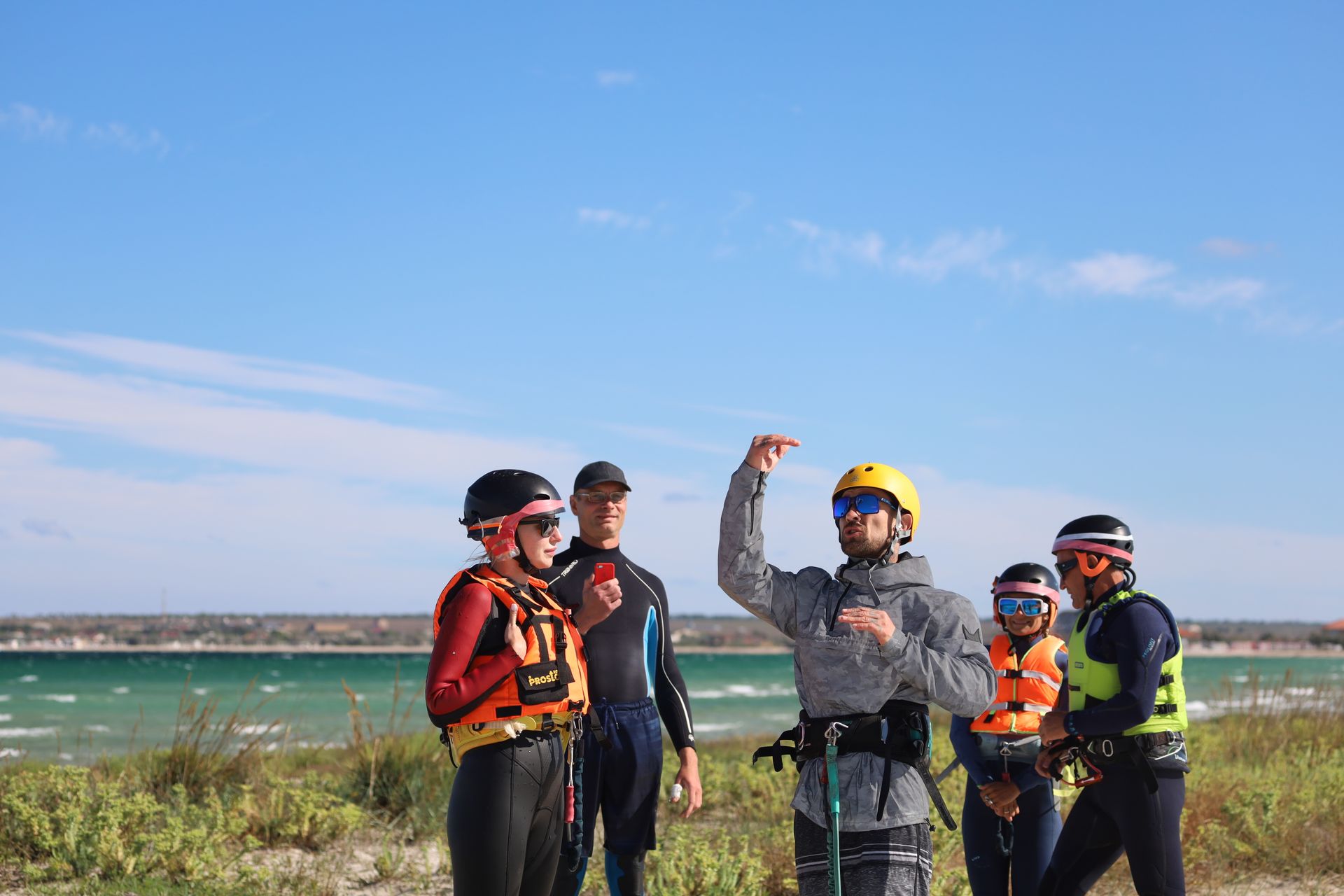 Kite surfing lesson with a group of adults wearing helmets and wetsuits on a sunny beach.