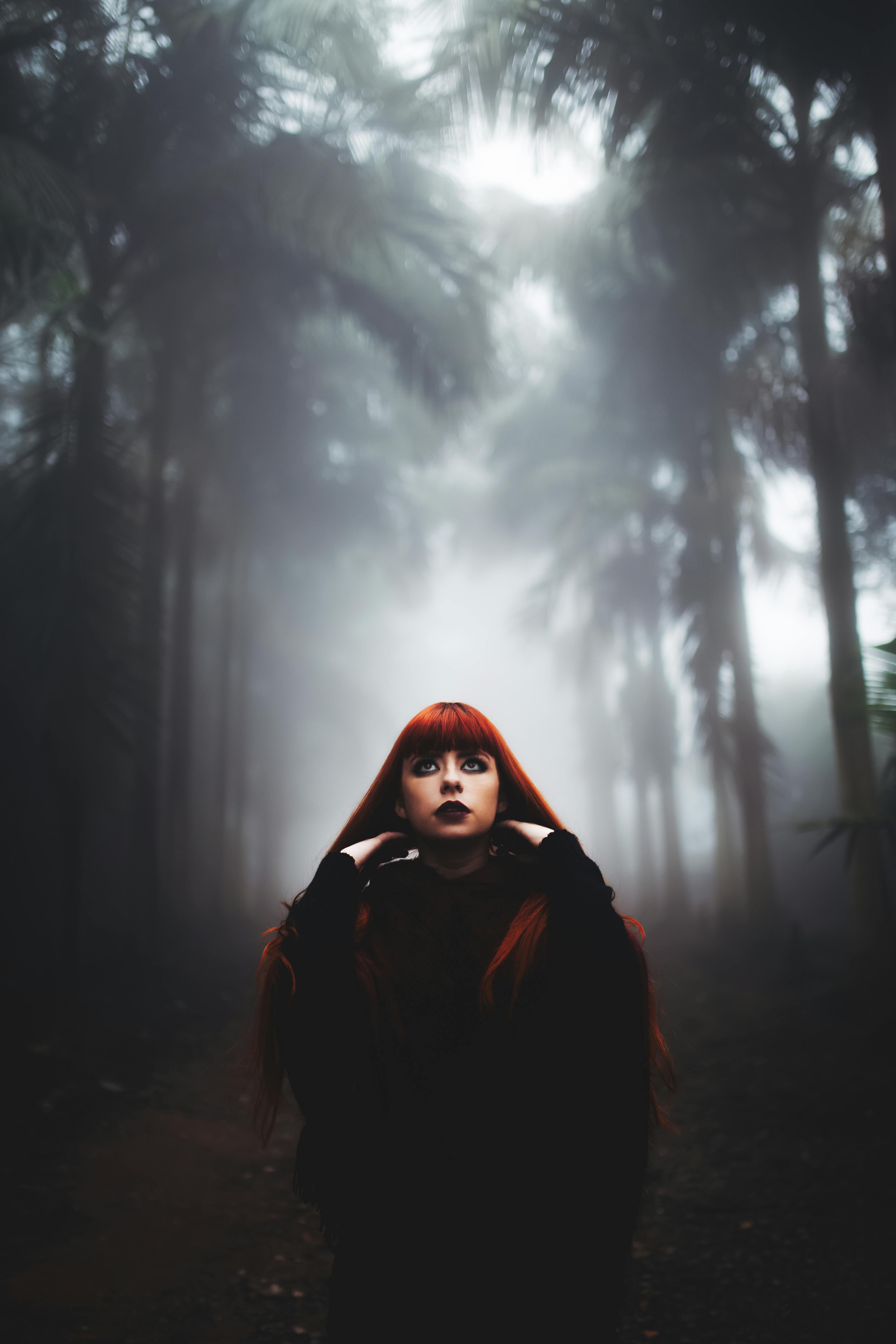 A woman with red hair posing in a foggy, mysterious forest scene.