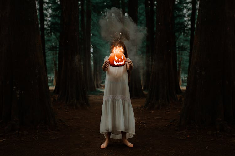 Woman In The Forest Holding A Carved Pumpkin Burning Inside 