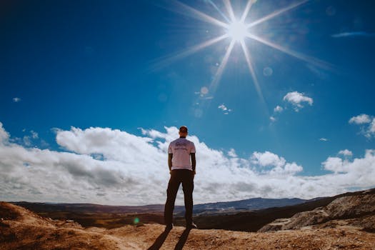 Silhouette of a man standing on a mountain top under a bright sun and blue sky.